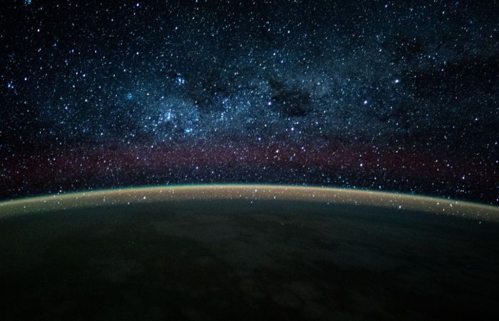The gently curved horizon of Earth emits a faint glow, with a dense blanket of stars in view above it.