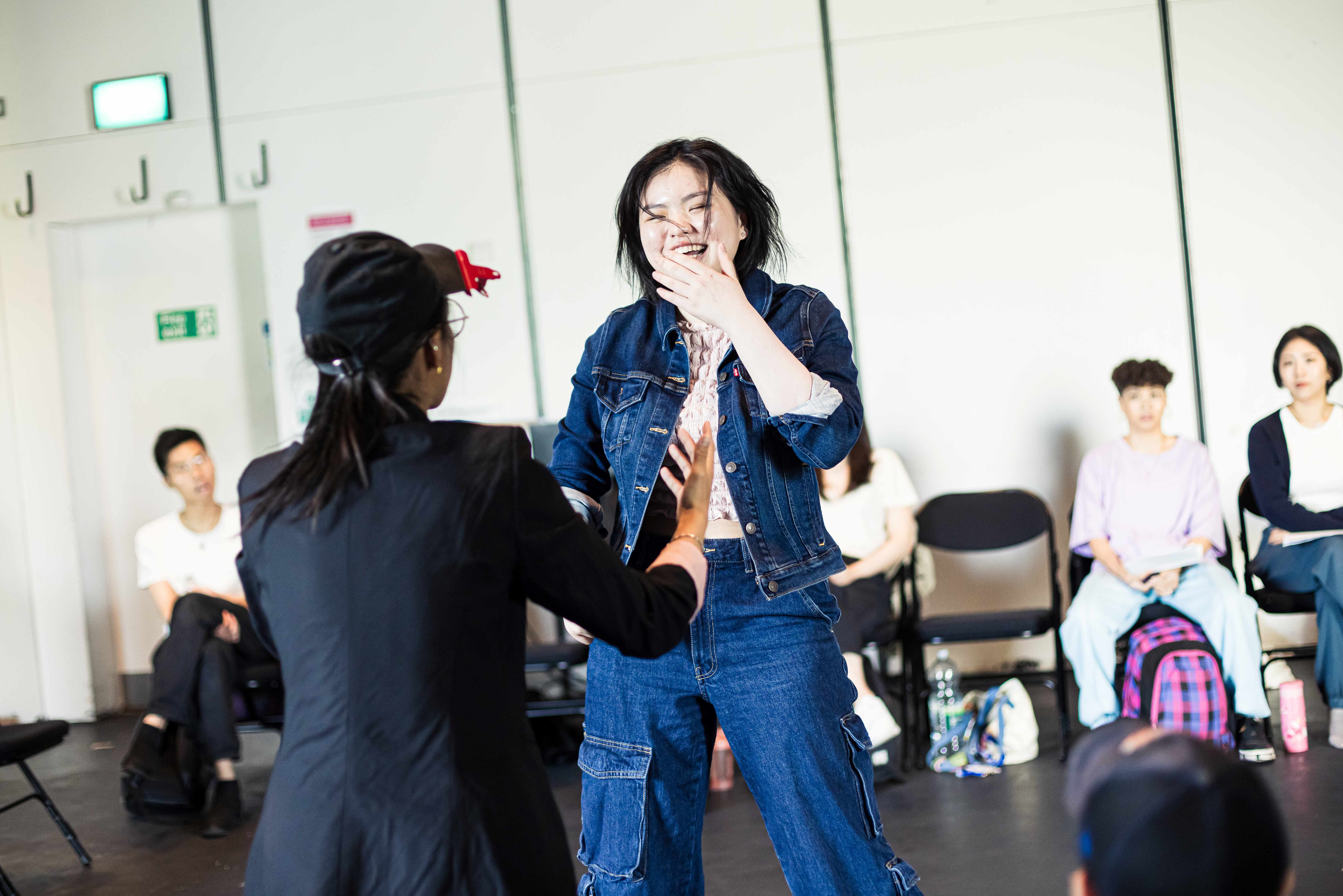 A picture of a room filled with BESEA artists receiving a workshop, with the focus point being a person laughing.