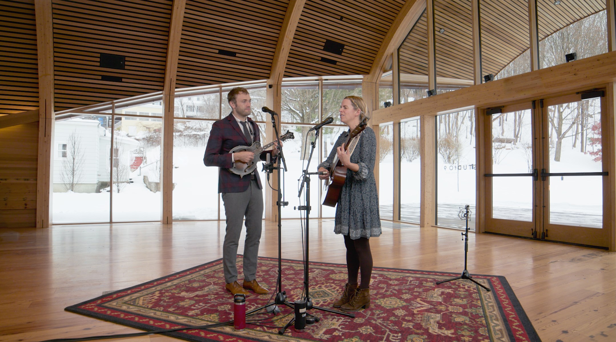 Chris Thile plays the mandolin, while Aoife O'Donovan sings and plays the acoustic guitar. They are standing inside Studio 9 in North Adams, MA