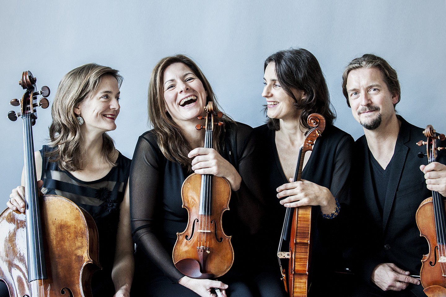 ID: Tetzlaff Quartet are standing in front of a grey backdrop. Each member is holding their respective instrument. Left to Right: Tanja Tetzlaff (violoncello), Elisabeth Kufferath (violin), Hanna Weinmeister (viola), Christian Tetzlaff (violin). Photo by Giorgia Bertazzi.