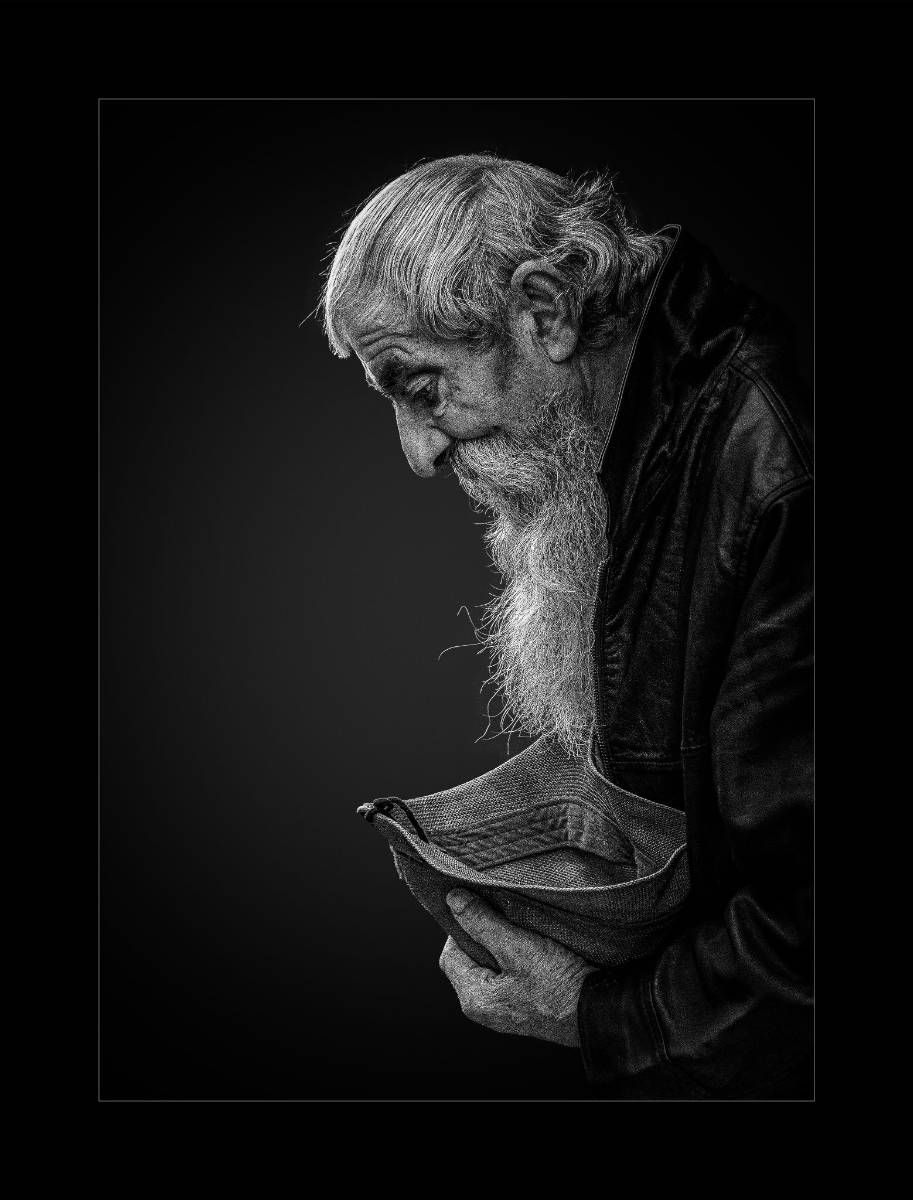 Black and white photograph of a man with a long white beard holding a hat