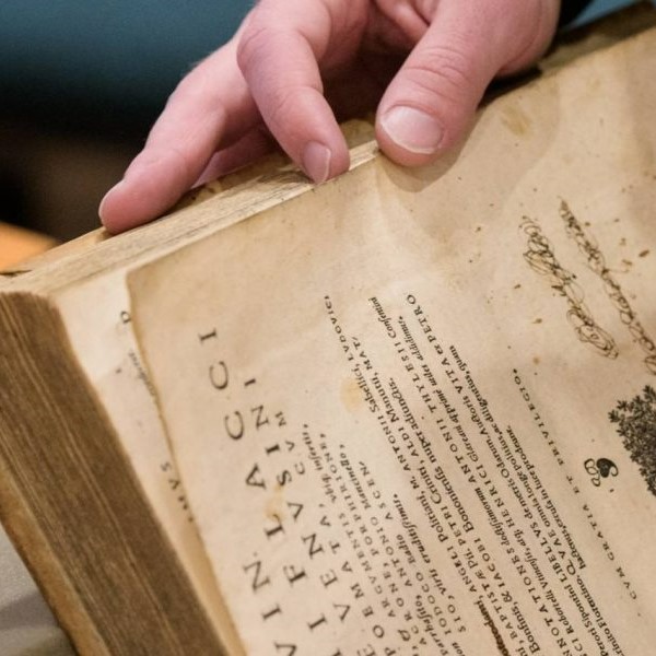 Photo of a hand holding open a rare book, propped up by foam pads