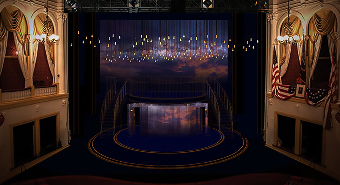 On the Fords Theatre stage sits a dark blue turntable outlined in gold. On either side, gold staircases lead up to a second level. From the ceiling, hundreds of incandescent bulbs hang glowing in front of a backdrop featuring a dark blue sky and pinkish clouds.On the Fords Theatre stage sits a dark blue turntable outlined in gold. On either side, gold staircases lead up to a second level. From the ceiling, hundreds of incandescent bulbs hang glowing in front of a backdrop featuring a dark blue sky and pinkish clouds. Link to set rendering. 