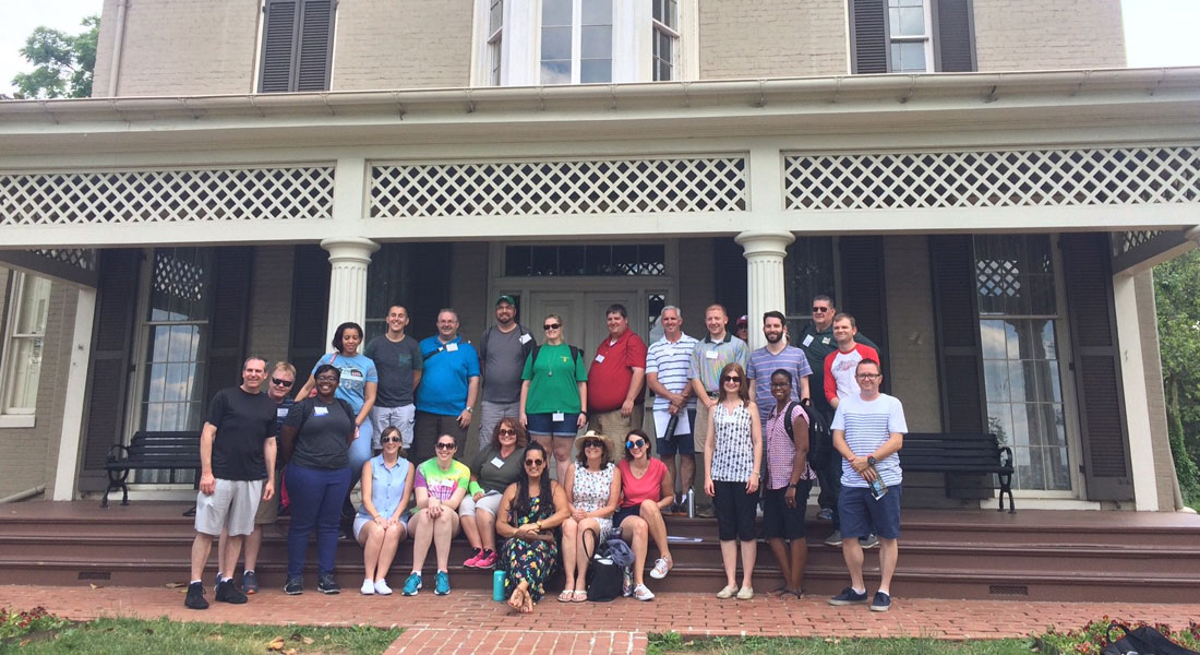 24 teachers gather, smiling, in front of a historic house. 