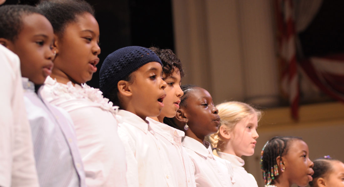 Nine elementary-age children in white tops stand in a line on the Ford''s Theatre stage. Link to watch now.