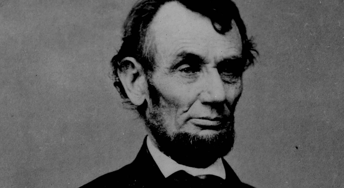 Abraham Lincoln, wearing his signature beard and a bow tie, looks directly into the camera. He is photographed from the chest up. Link to Abraham Lincoln Symposium.
