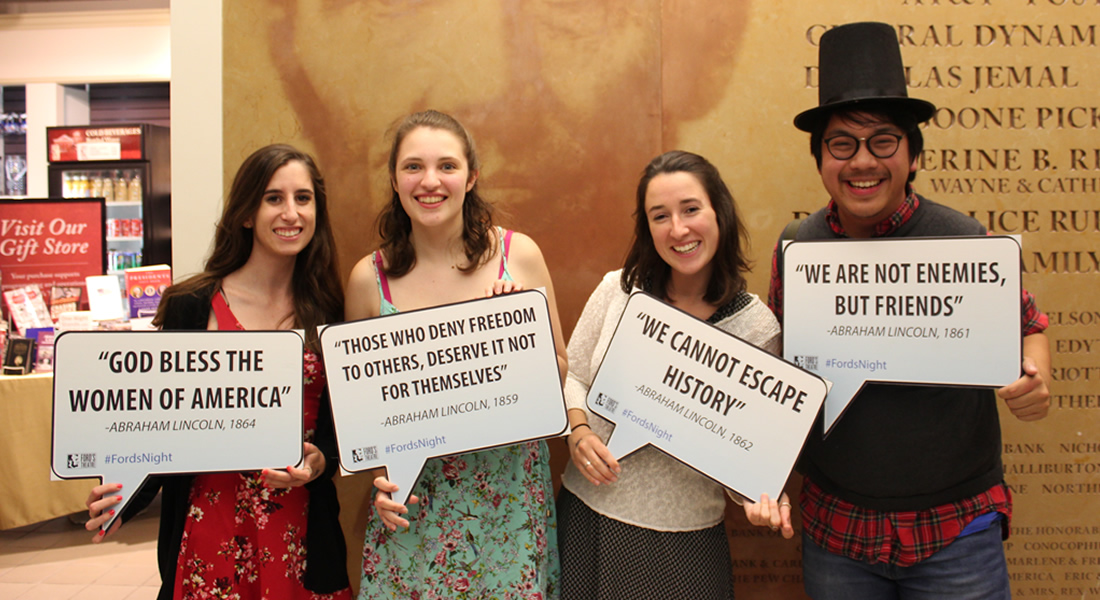 Four people hold signs with famous quotes by Abraham Lincoln. 