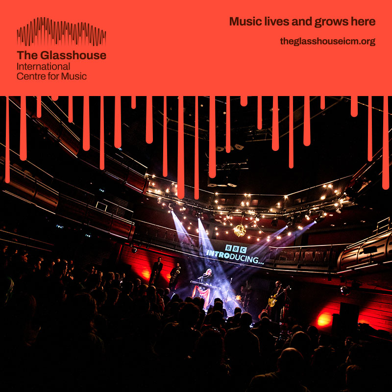 Ernie: a band of five people are performing on stage with red lighting behind them. A girl with blonde hair is singing and playing a keyboard, one is playing an electric guitar, two are playing brass instruments, and one is playing drums at the back