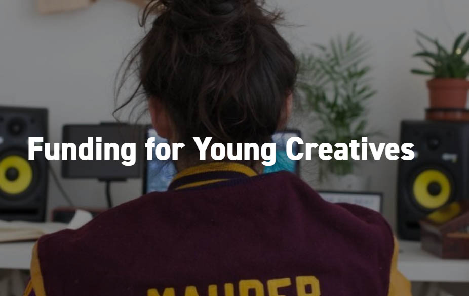 A young woman with brown hair tied up is looking away from the camera at a laptop on a desk. The wording 'Funding for Young Creatives' is written in white over the top