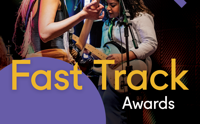 Two young women are in the background of the image, they are both playing electric guitars. The young woman on the right has dark hair and a long-sleeved jacket on. You can't see the young woman's face on the right, only her arm playing the guitar. The wording 'Fast Track Awards' is at the forefront of the image.
