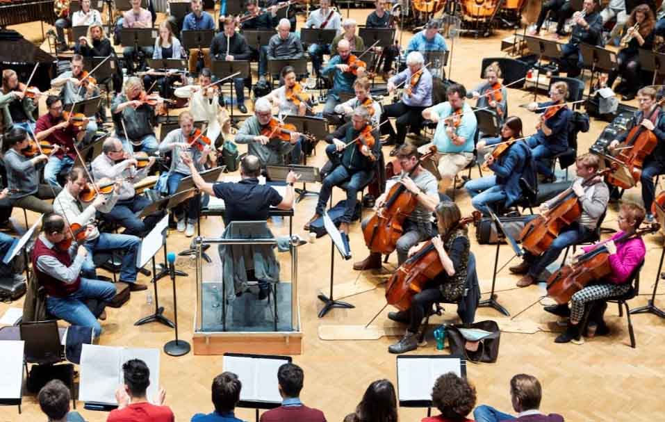 A full orchestra. The right hand side of the image shows about 20 people of all ages playing cello, and the left hand side of the picture shows about 20 people of all ages playing violin.