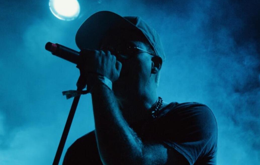 A young male is singing into a microphone. He is wearing a cap and dark coloured t shirt