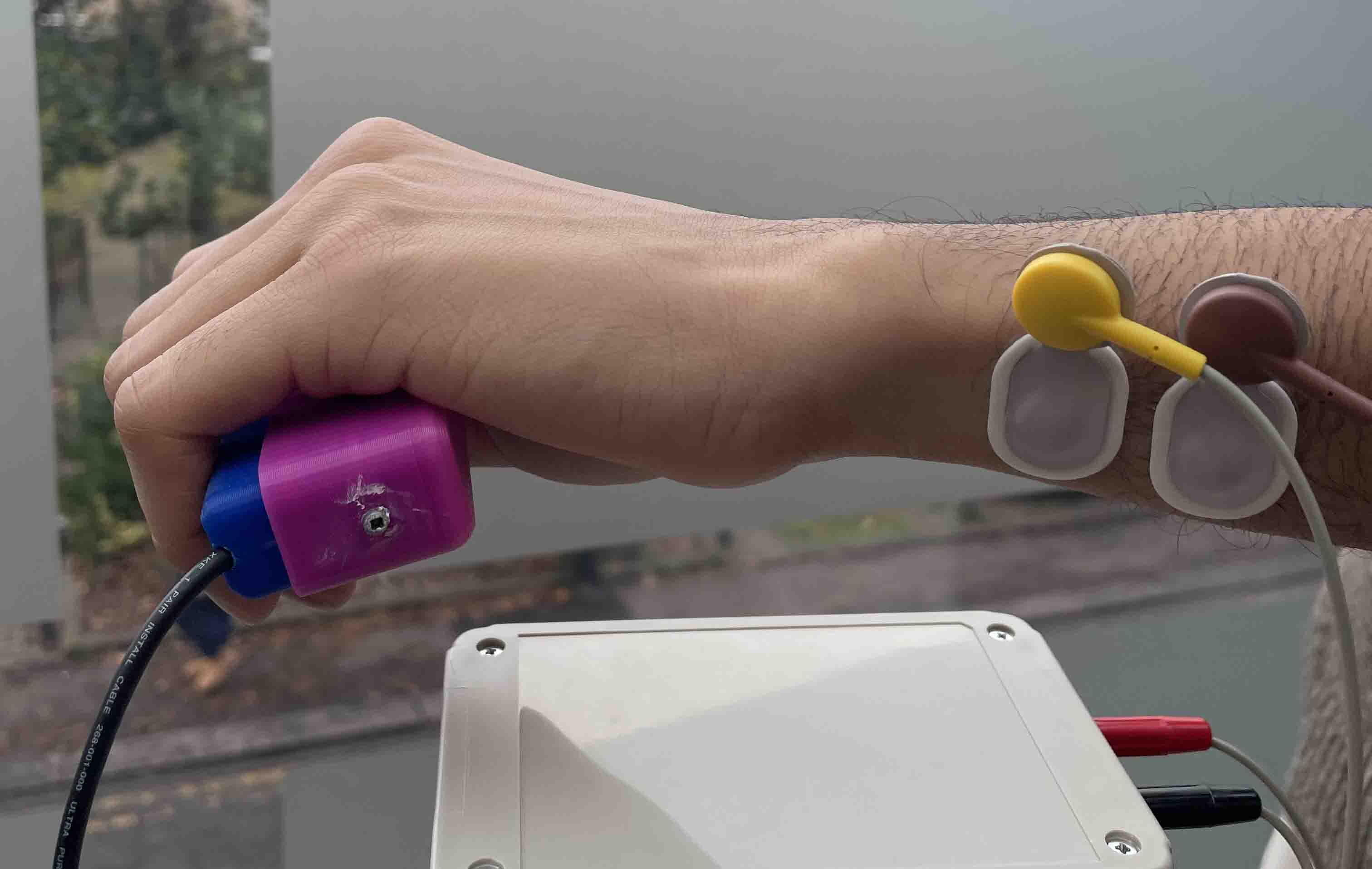 A hand holding a medical device with some wires stuck to the wrist