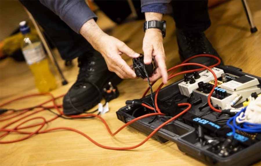 Picture of a person plugging into a guitar pedal rack