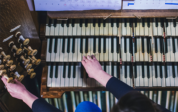 Shows two hands playing an organ, with sheet music located directly in front