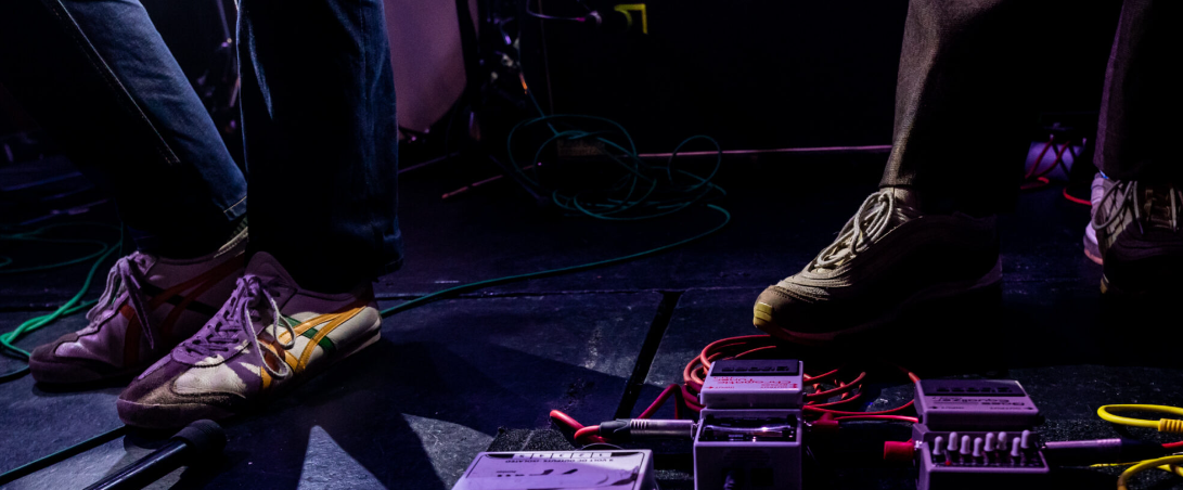 two pairs of feet on stage with guitar pedals