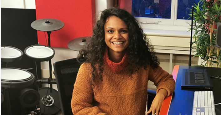 Xylo Aria in her studio smiling wearing an orange jumper