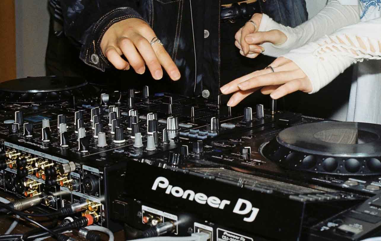 Two people are seen using DJ decks