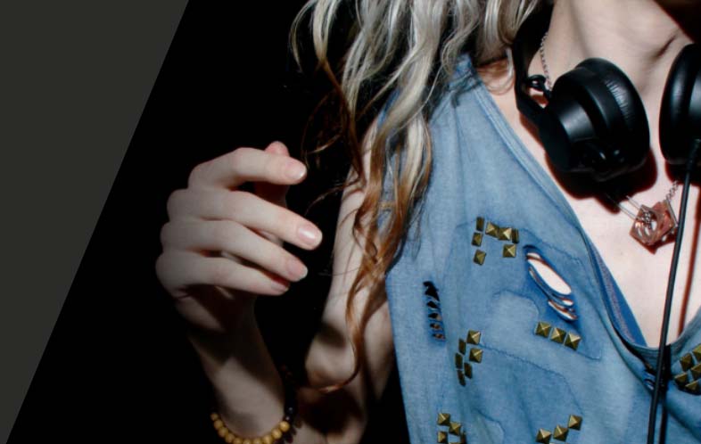 A young woman's blue top is visible. Her blonde hair is covering her shoulders and she is wearing black headphones round her neck