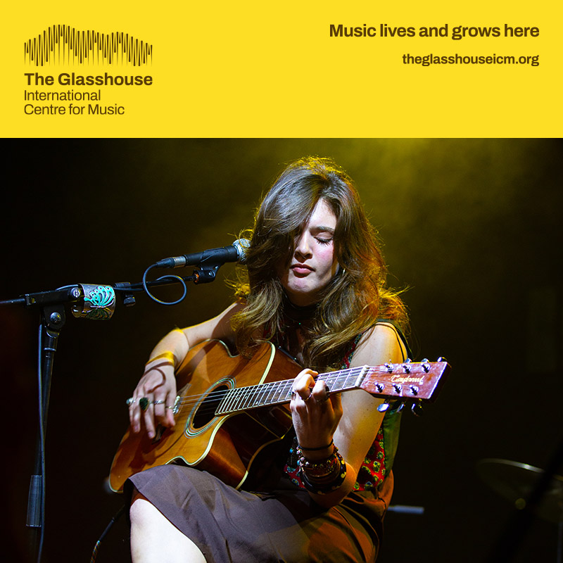 Anna Karila: a young girl with brown hair is sat down playing acoustic guitar