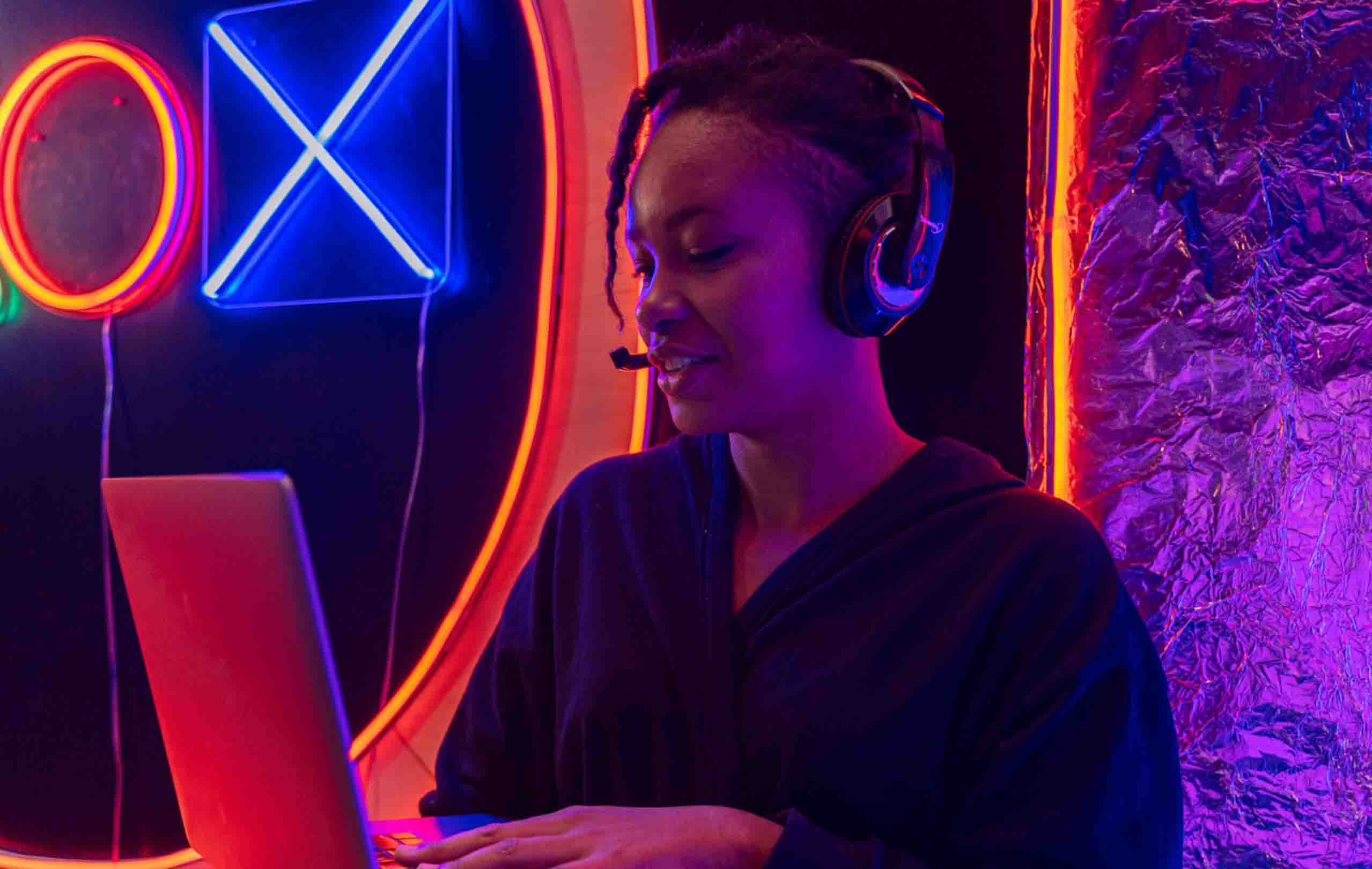 A young person is seen with a headset on and typing on a laptop
