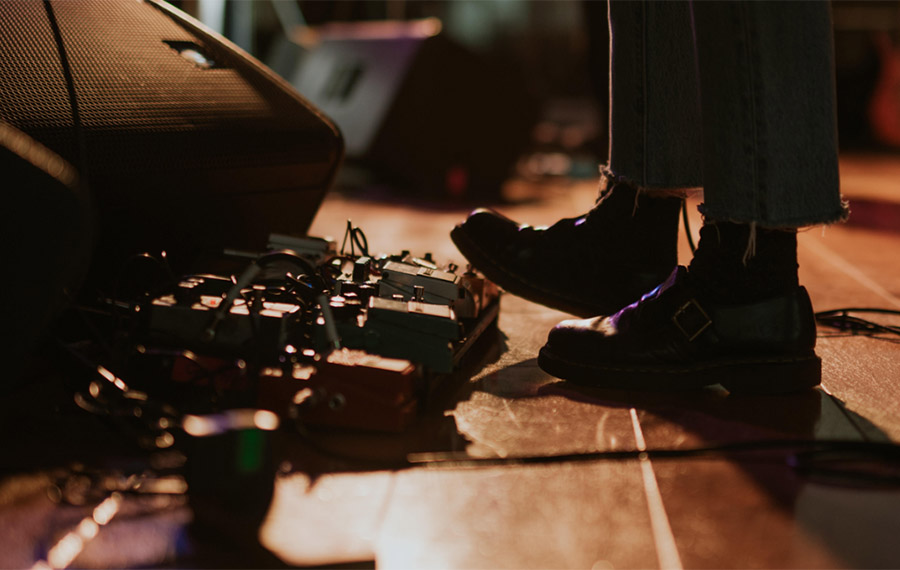 Someone is wearing black shoes and using a guitar pedal board