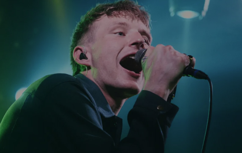 A young man is singing into a microphone. He has blonde hair