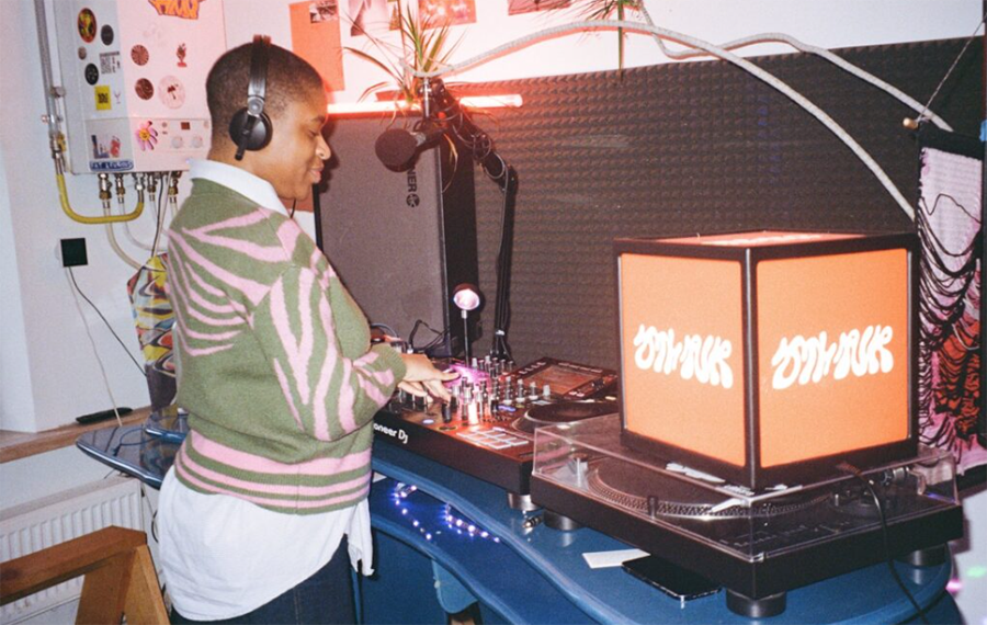 A woman is stood in front of DJ decks and wearing headphones