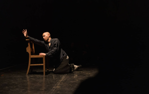 A person is laid next to a chair and reaching out over the top