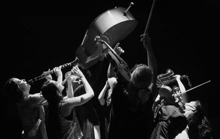 A group of musicians are all seen lifting up a double bass in the air