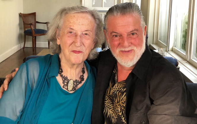 An older man and a woman are sat side by side staring and smiling at the camera