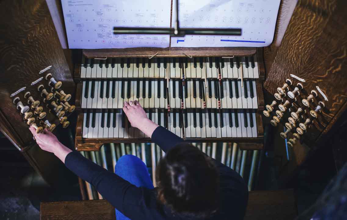 A young woman is seen playing an organ with sheet music above