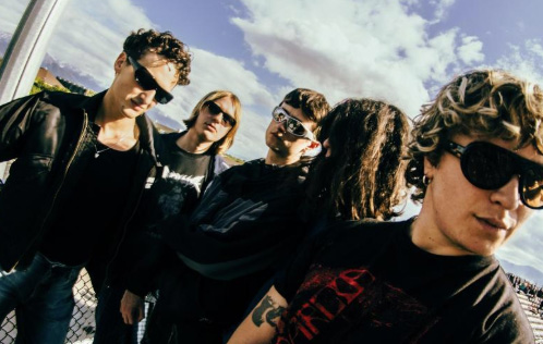 Five people are all wearing sunglasses and staring at different points away from the camera