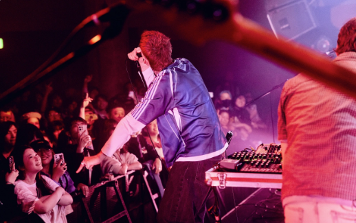 A young guy is performing on stage and a crowd is in front of him. He is wearing a blue t shirt