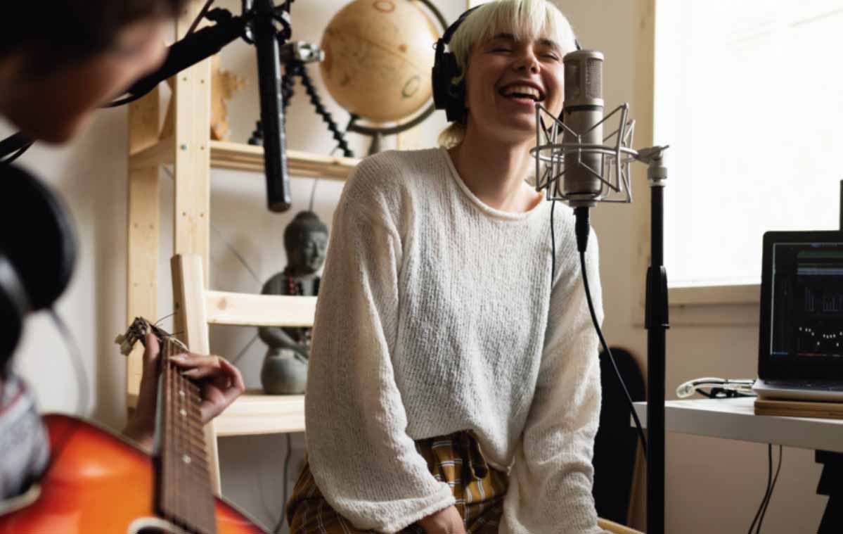A young woman with blonde hair is singing into a microphone with headphones on