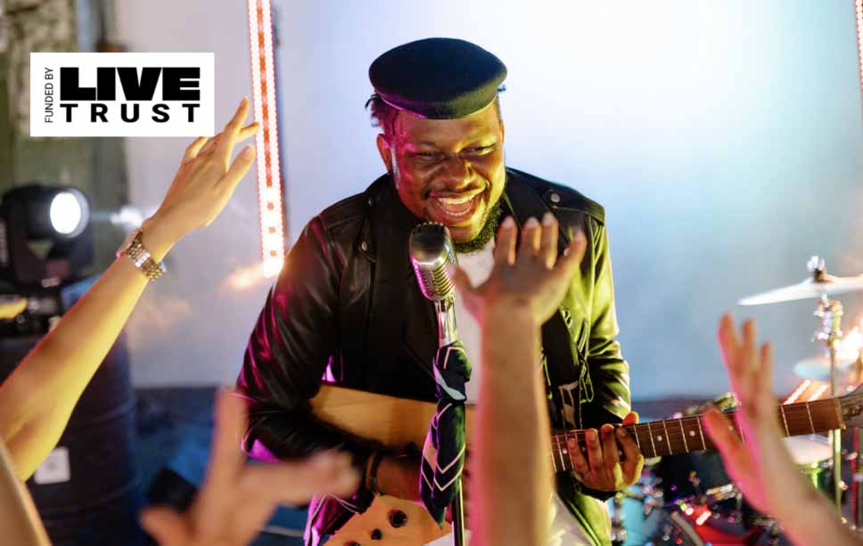 A young man with a hat on is playing electric guitar in front of an audience