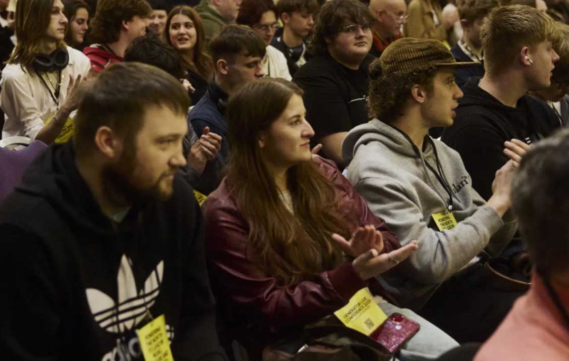 People are seen sat in a row staring at a stage