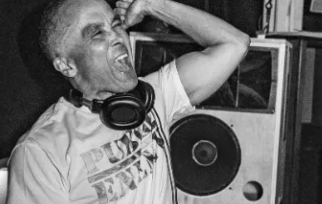 A man with headphones around his next is shouting with his hand in the air