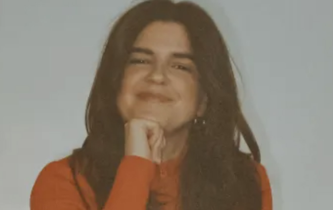 A young woman with long brown hair is staring straight into the camera. 