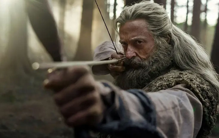 An old man with white long hair is holding a bow and arrow and staring just past the camera