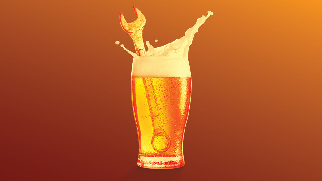 A pint of beer with a wrench dropped inside sits centers on a brown and yellow gradient background.