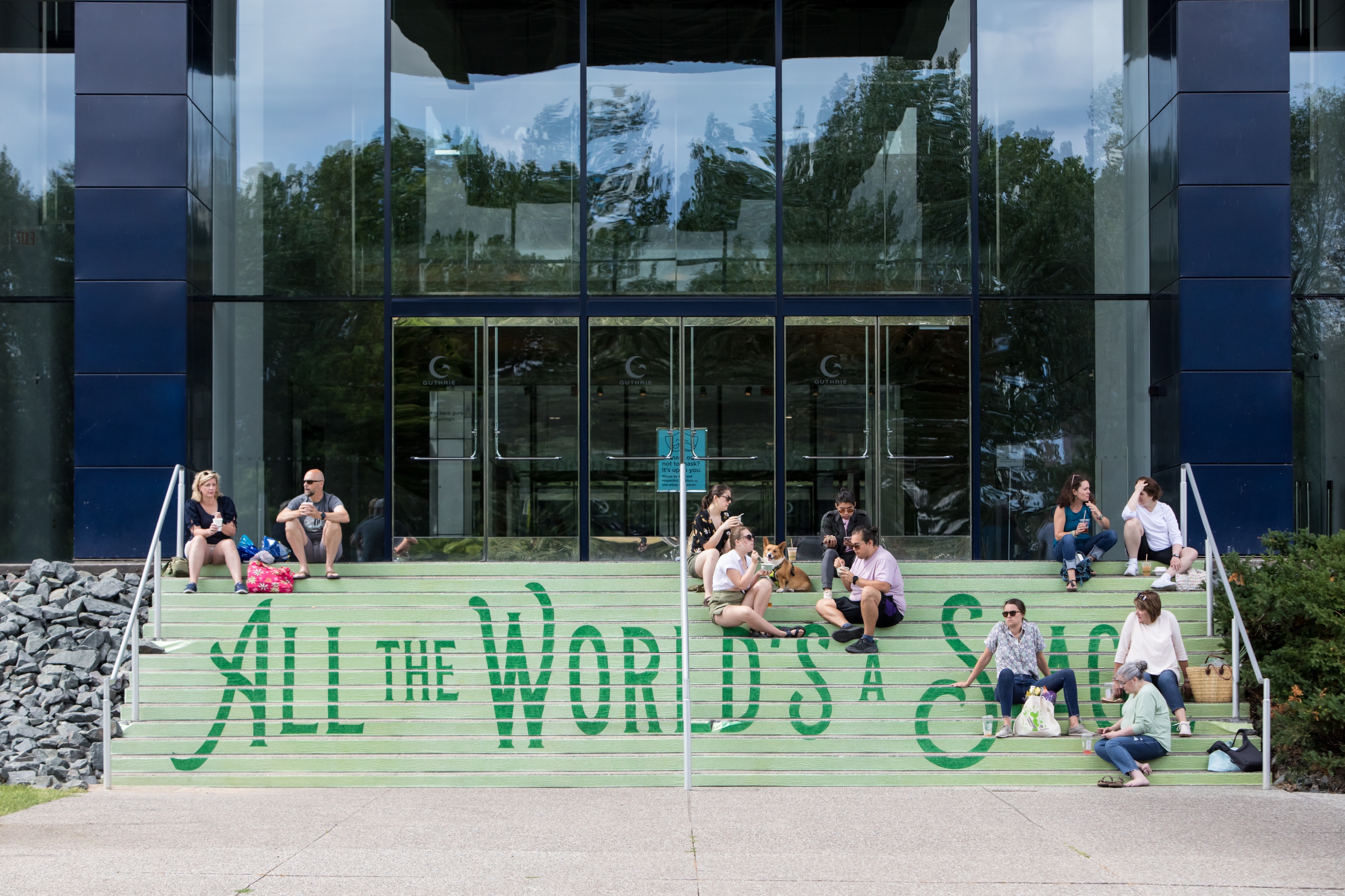 A photo of the exterior of the Guthrie building and stairs. The stairs are painted green with the words, "All the world's a stage". 