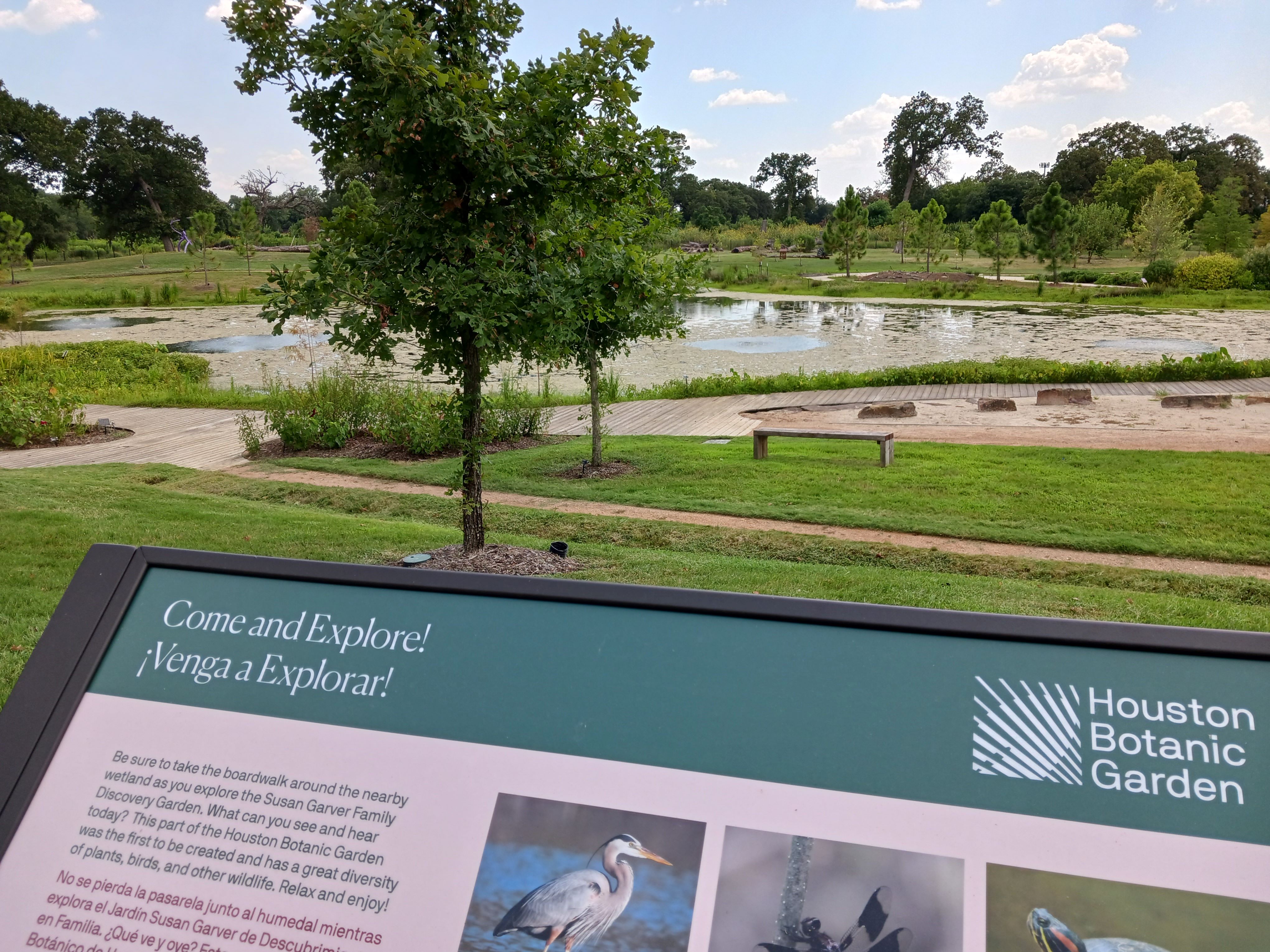 New placemaking signage with greenery, a walkway, and pond in the background. 