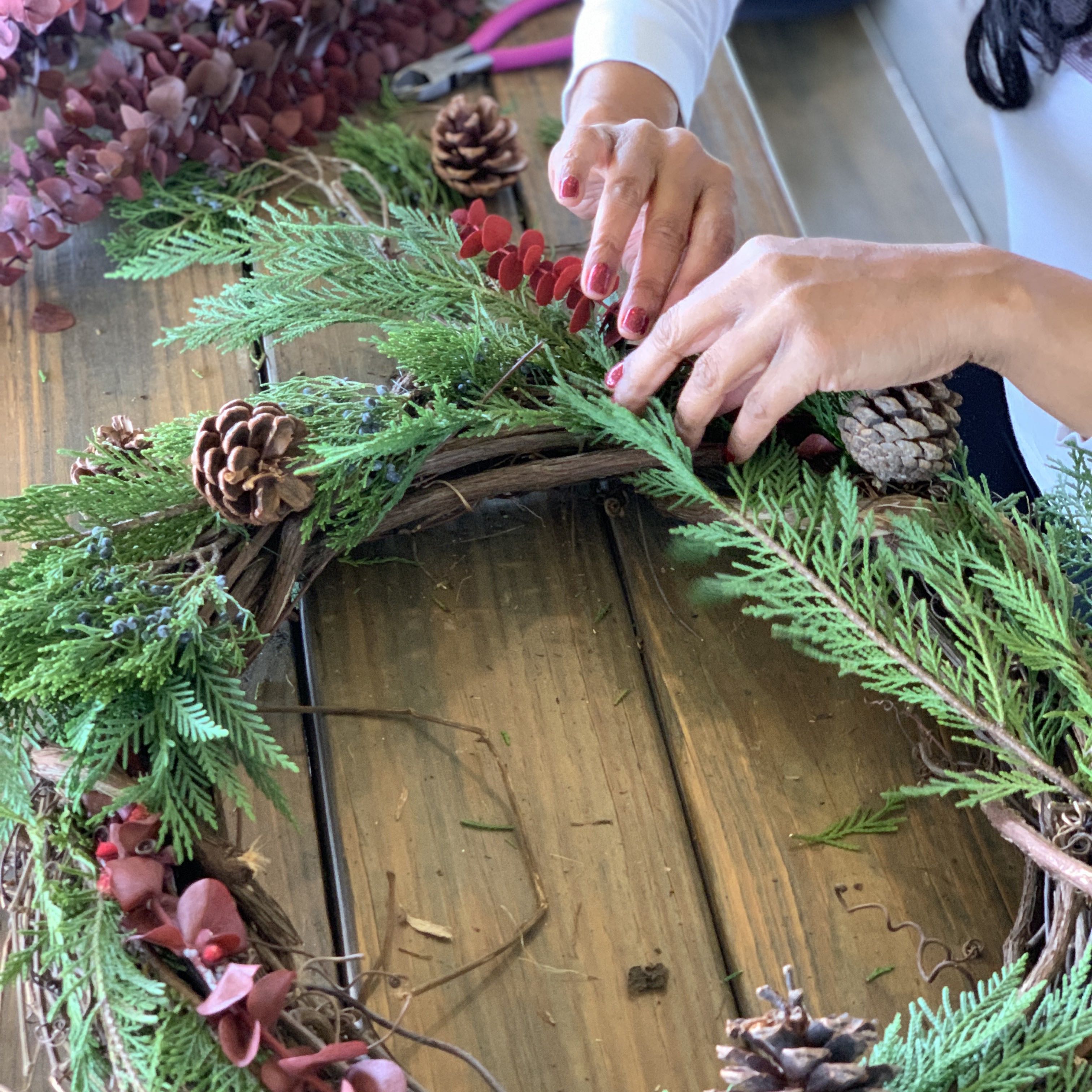 Woman makes a wreath by hand on a wooden tabletop.