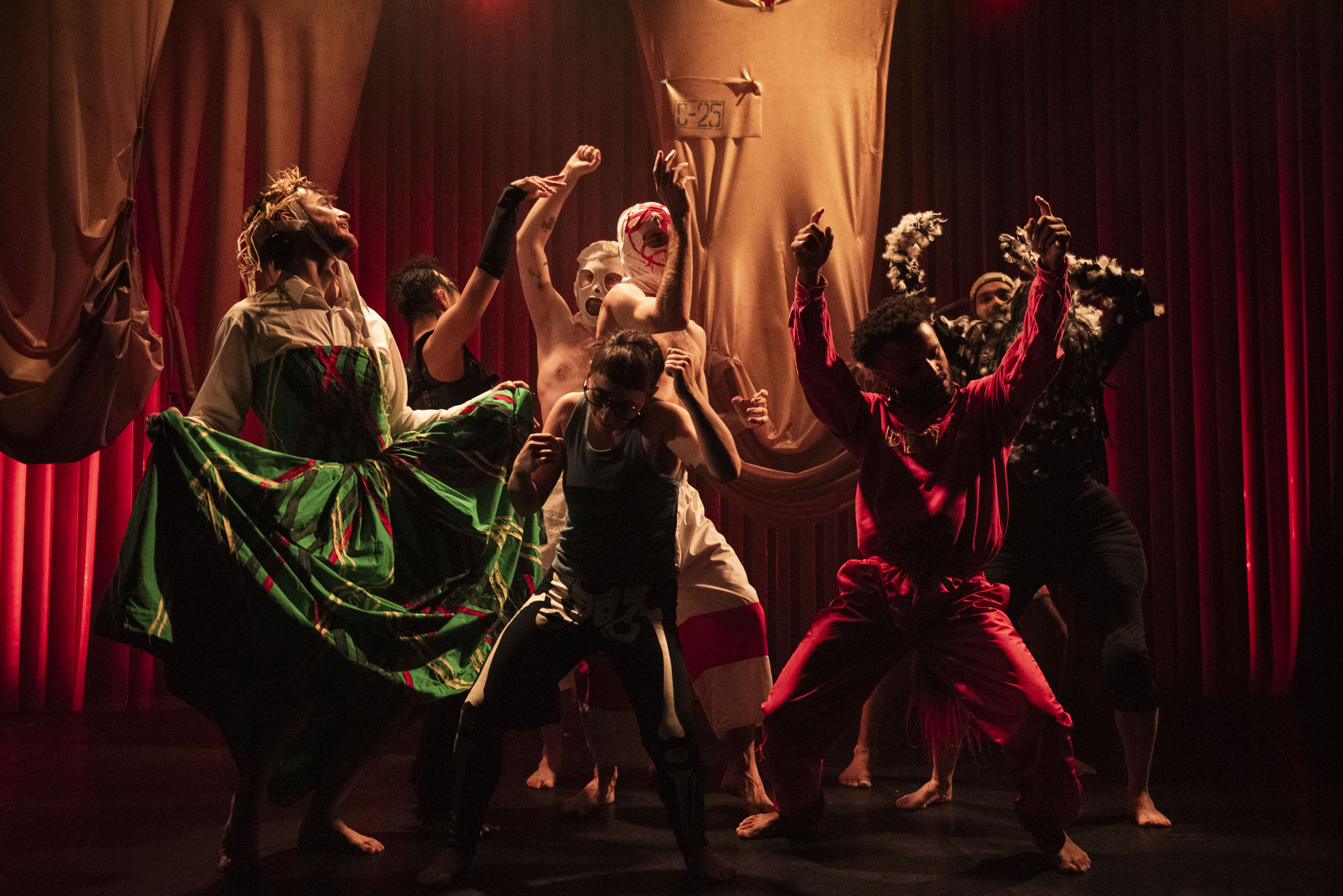 The character Specky is surrounded by an ensemble of dancers in eclectic, folklore-inspired costumes during a dynamic scene.