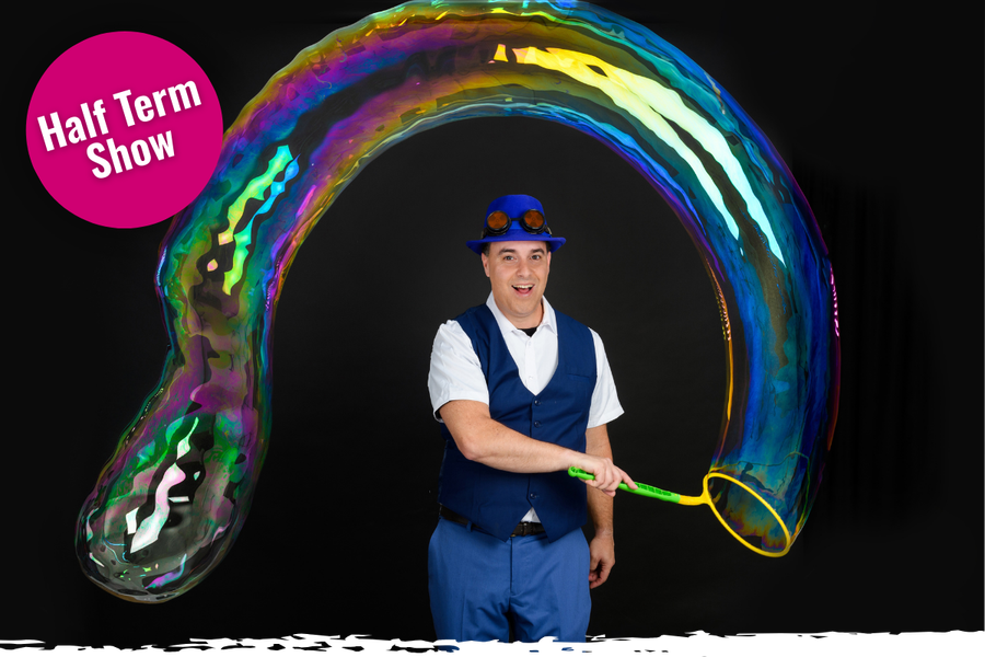 A person waves a large bubble wand, and a long colourful bubble streams over his head.