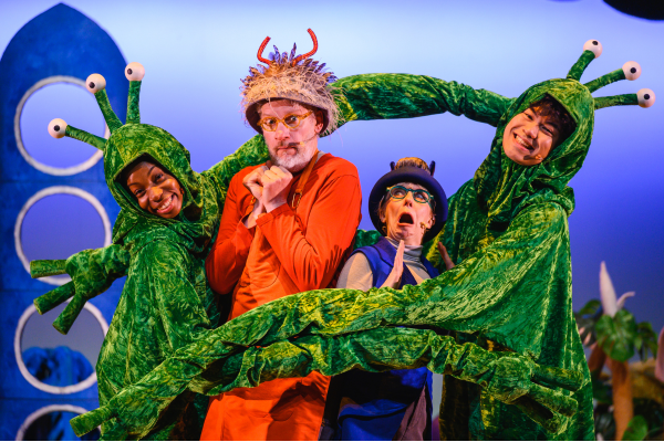 Four people dressed as aliens stand on a stage