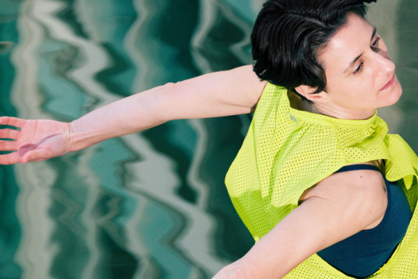 A woman running with her arms flung backwards, wearing a yellow mesh top