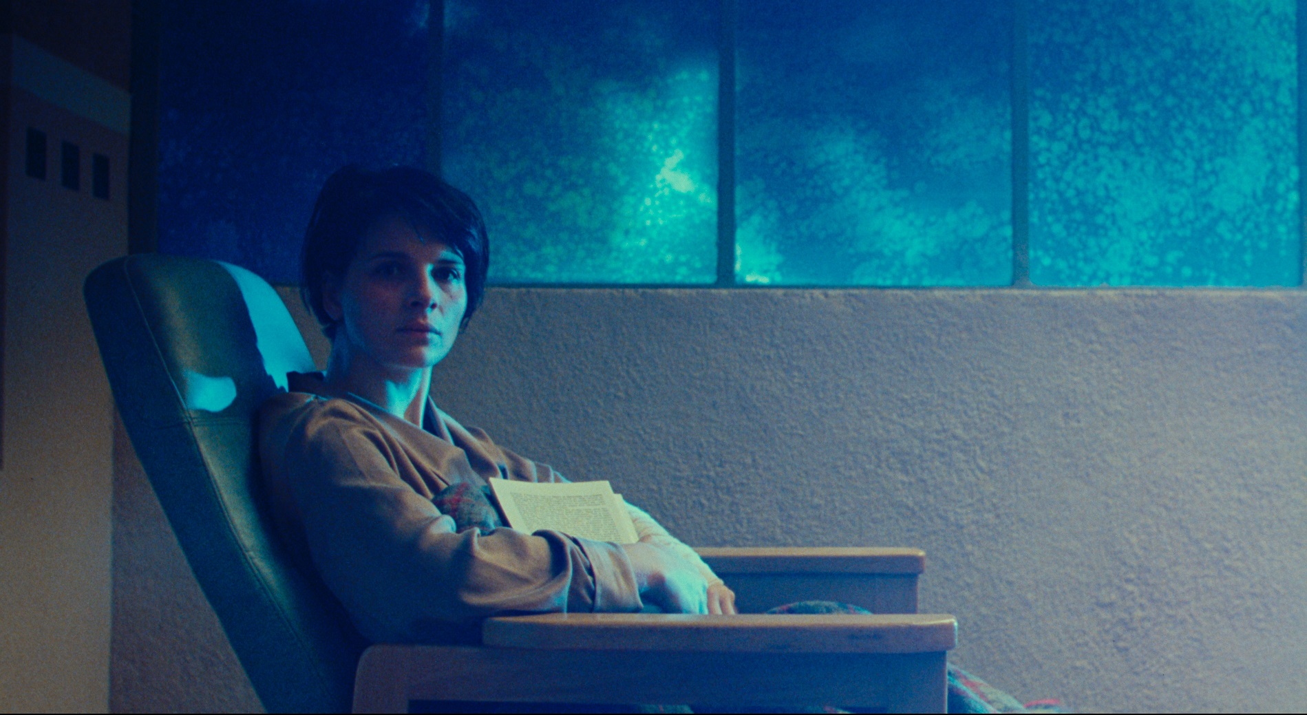  A woman sits on a reclining seat, bathed in blue light and shadow. 