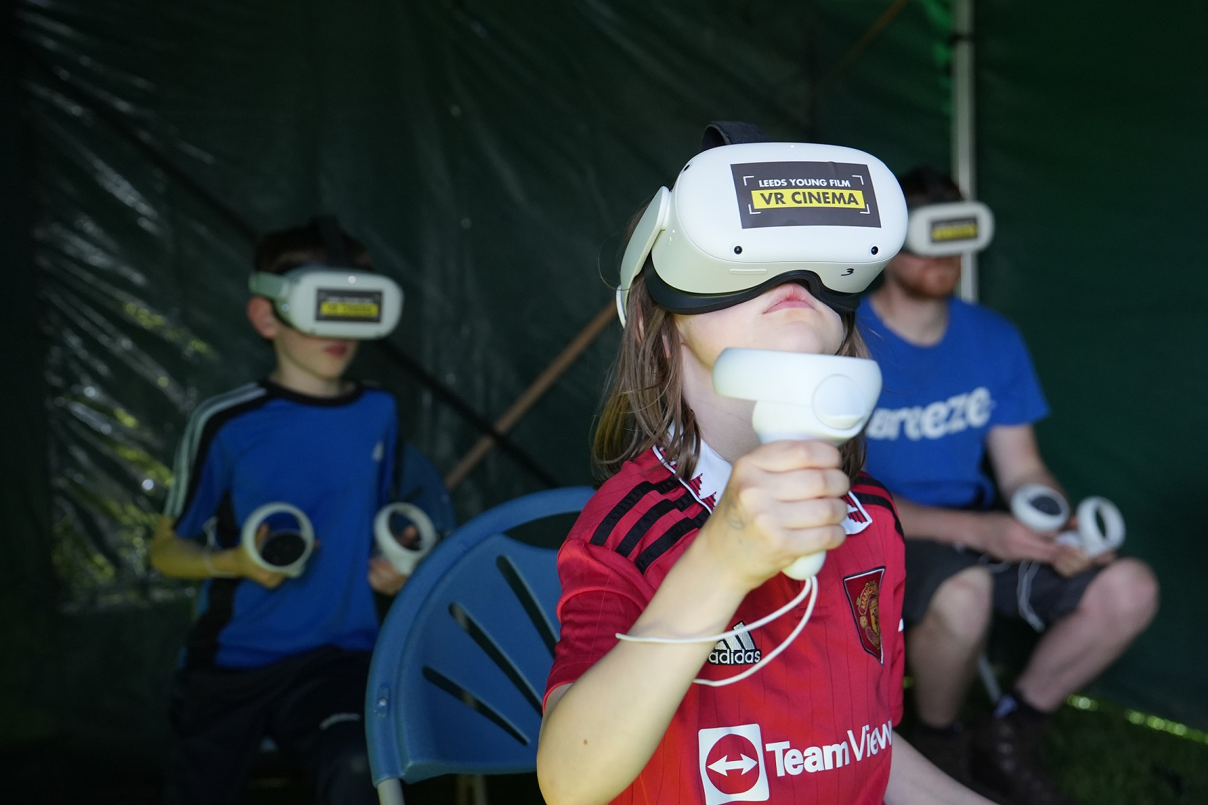 A young boy sits in a darkened marquee with a VR Headset on that reads: LEEDS YOUNG FILM VR CINEMA
